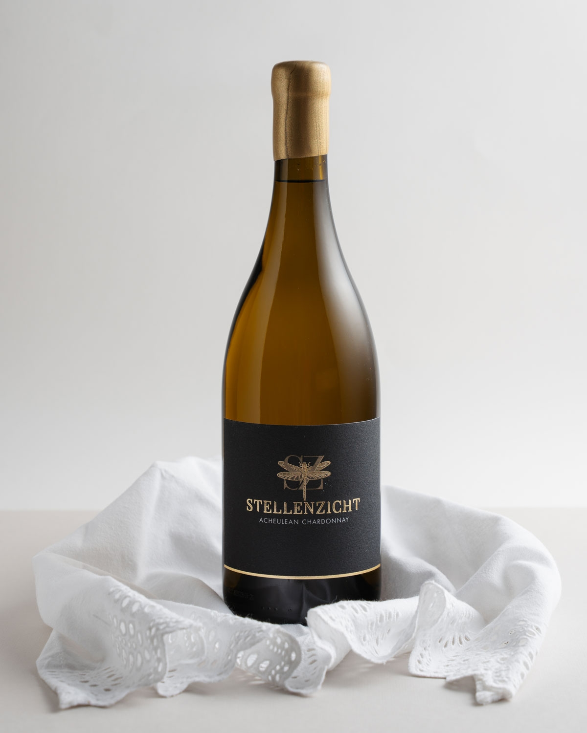 Weinflasche mit Goldfolienverschluss und schwarzem Etikett mit goldenem Libellenmotiv und dem Text STELLENZICHT ACHEULEAN CHARDONNAY in goldener Schrift.