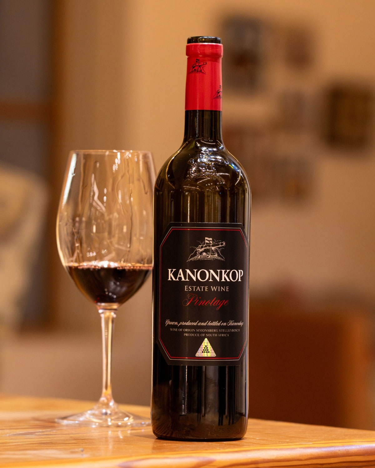 Eine Flasche Kanonkop Estate Wine mit einem dunklen Etikett, roter Folie am Hals und einem Text, der darauf hinweist, dass es sich um einen Pinotage aus Stellenbosch, Südafrika, handelt, mit einer Kanonenillustration auf dem Etikett.
