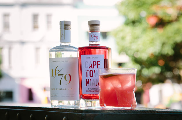 Two bottles of gin and a glass with a red cocktail on an outdoor table