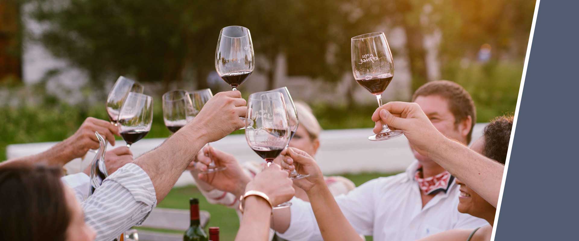 People celebrating outdoors at sunset, raising their red wine glasses for a toast