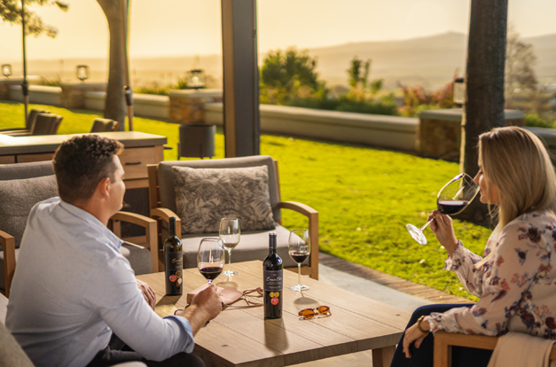 Paar genießt bei Sonnenuntergang Rotwein auf einer Terrasse mit Blick auf die Landschaft