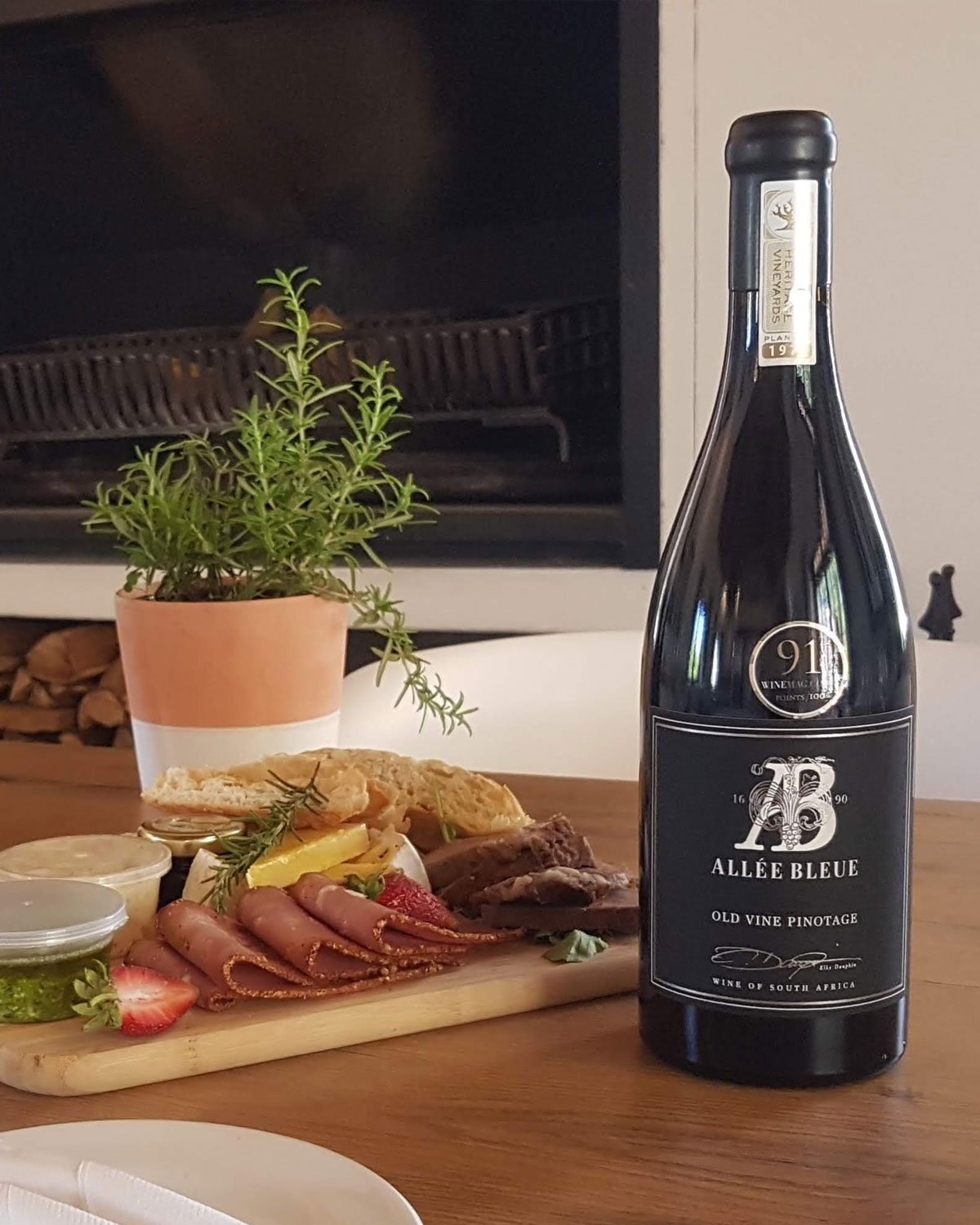 Eine Flasche Allée Bleue Old Vine Pinotage mit einem schwarzen Etikett mit silbernem Prägetext und einem Siegel am oberen Rand des Halses. Das Etikett enthält dekorative Schriftzüge und die Herkunft PIEKENIERSKLOOF.