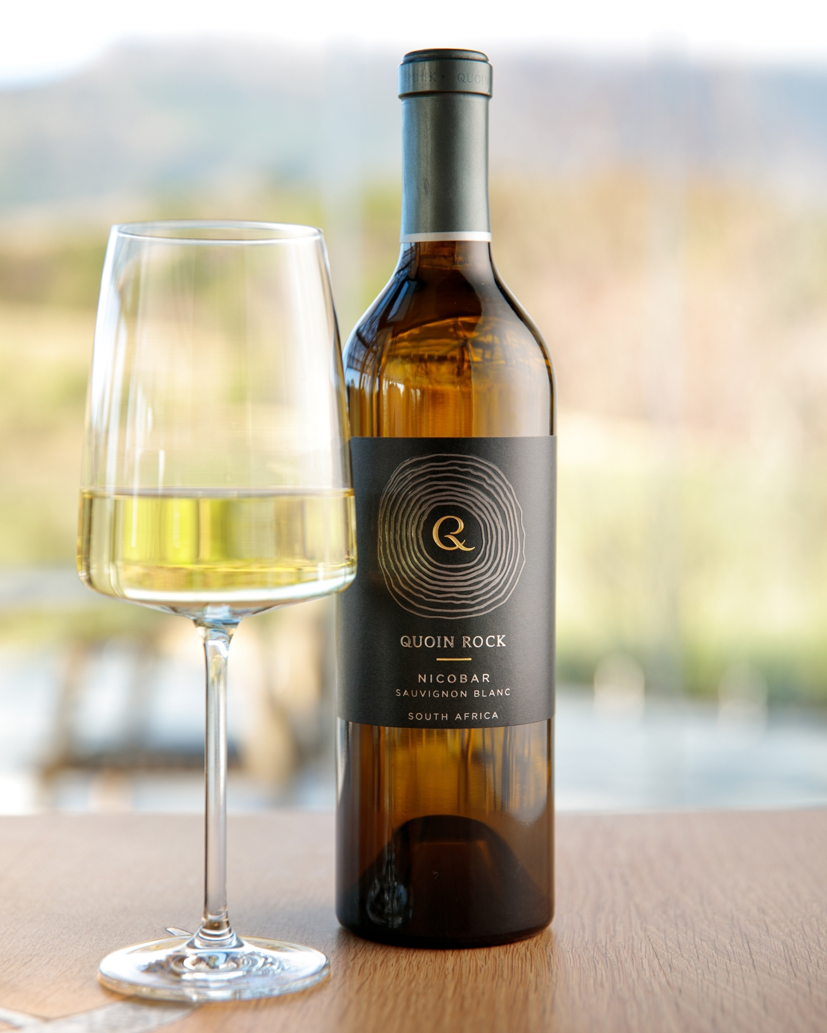 Eine Flasche Quoin Rock Nicobar Sauvignon Blanc aus Südafrika mit grünem Folienverschluss und dunklem Etikett mit goldener und weißer Schrift und kreisförmigem Muster.
